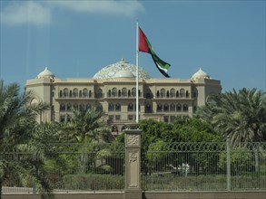 An imposing palace with a waving flag and surrounded by palm trees, abu dhabi, united arab emirates