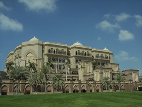 Magnificent palace with palm trees and green lawn under a clear sky, abu dhabi, united arab