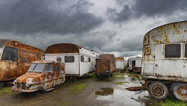 Abandoned caravans and vehicles under a gloomy, cloudy sky, rainy and desolate atmosphere, symbolic
