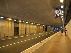 An illuminated tunnel with a road and pavements, people walking along the pavement, monte carlo,