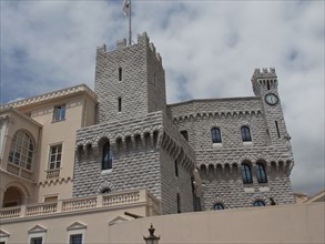 A historic castle with stone towers, windows and a clock, against a cloudy sky, monte carlo,