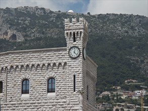 A stone tower with a clock against a mountain backdrop and cloudy sky, monte carlo, monaco, france
