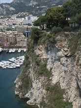 Cliffs overlooking the marina, the city and mountains, with lush greenery and rocky slopes, monte