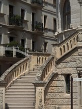 Stone staircase with ornate balustrade in front of historic buildings with balconies and ornate