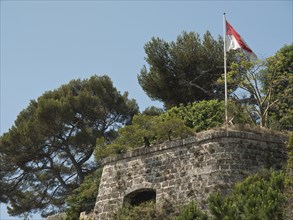 An old stone wall with a red and white flag and surrounded by trees and green vegetation, monte