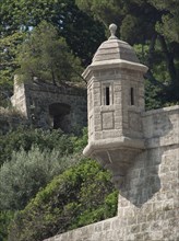 A historic watchtower made of stone, surrounded by trees and green vegetation, part of an old