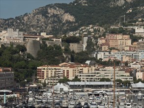 City view with medieval fortress on a hill surrounded by modern buildings and a marina, monte