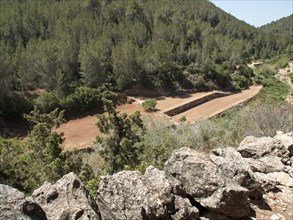 View of a wooded area and a rural valley with rocky structures in the foreground, surrounded by