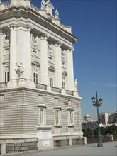 Corner view of a magnificent palace with several sculptures and columns, and a street lamp against