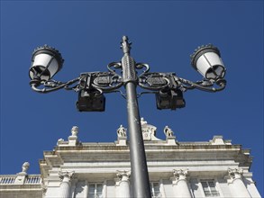 Close-up of a wrought-iron street lamp in front of a historic building under a blue sky, Madrid,