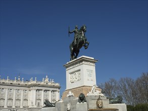Historical monument with an equestrian statue in front of a palace and blue sky, Madrid, Spain,