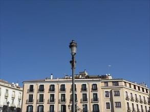 Urban lantern in front of a building with balconies, blue sky and roofs, Madrid, Spain, Europe