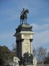 Equestrian statue on a high pedestal under a blue sky, surrounded by trees, Madrid, Spain, Europe