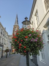 Quiet old town street with street lamp and flower decoration, church in the background under a