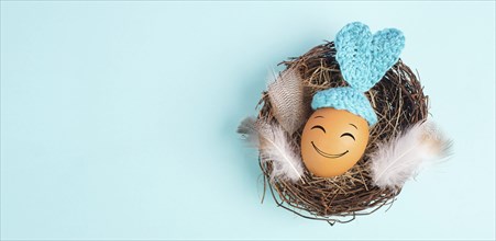 Easter bunny or rabbit egg in a bird nest, crocheted ears and feathers, spring holiday, blue color