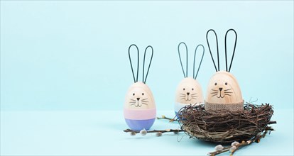 Easter bunny or rabbit sitting in a bird nest, willow branches, wooden egg, spring holiday, blue