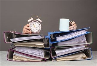 Exhausted tired woman with coffee and alarm clock, pile of file folders, burnout, stress and