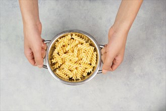 Cooked fusilli pasta in a sieve or strainer, italian food ingredients, hands holding colander