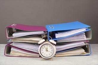 Alarm clock standing next to pile of file folders, burnout, stress and overworked, pressure at