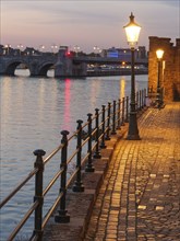 Dusk on the river bank with cobblestones and illuminated street lamp, Maastricht, limburg,