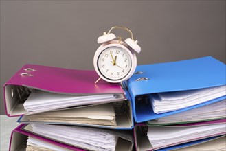 Alarm clock standing on pile of file folders, burnout, stress and overworked, pressure at work,