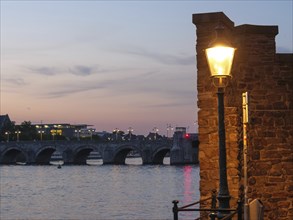 Atmospheric dusk at a bridge with illuminated street lamp and river, Maastricht, limburg,
