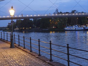 River bank at dusk with illuminated lantern and bridge in the background, reflections in the water,