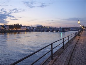 Full length shot of a river at dusk with a bridge and houses in the background, illuminated