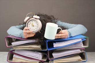 Exhausted tired woman with coffee and alarm clock, pile of file folders, burnout, stress and