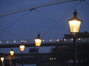 Close-up of illuminated lanterns along a footpath at night with an illuminated bridge in the