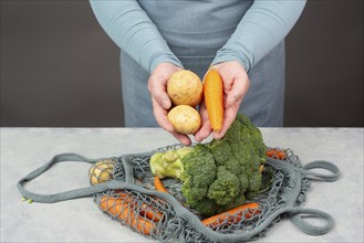 Hands taking potato from the mesh bag with vegetables, shopping grocery, healthy food ingredients,