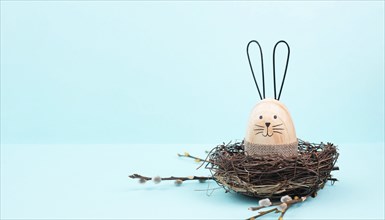 Easter bunny or rabbit sitting in a bird nest, willow branches, wooden egg, spring holiday, brown