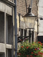 Detailed view of an old building façade with hanging lamp and blooming flowers, Maastricht,