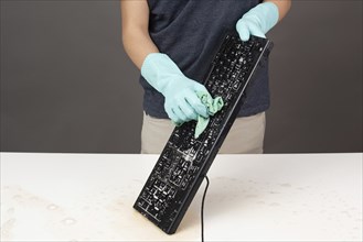 Cleaning computer keyboard in office with rubber protective glove, whiping with water and soap,
