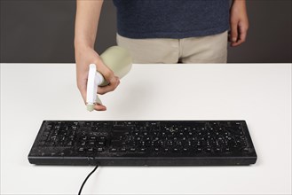 Cleaning computer keyboard in office, spraying water with a spray bottle dusty and dirty