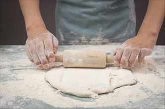 Baker rolls out dough for pizza, flatbread or pastry with rolling pin, prepare ingredients for