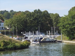 Marina with boats on the riverbank, surrounded by green trees in sunny weather, Maastricht,