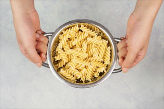 Cooked fusilli pasta in a sieve or strainer, italian food ingredients, hands holding colander