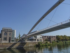 View of a modern bridge over a river with neighbouring urban buildings and blue sky, Maastricht,