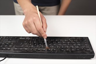 Cleaning computer keyboard in office with rubber protective glove and a brush, dusty and dirty