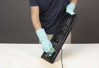 Cleaning computer keyboard in office with rubber protective glove, whiping with water and soap,