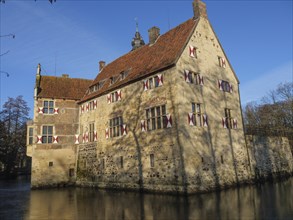 An old moated castle with red shutters and a red roof, surrounded by water, lüdinghausen,