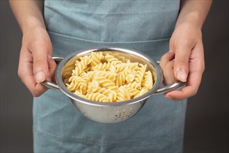 Cooked fusilli pasta in a sieve or strainer, italian food ingredients, hands holding colander