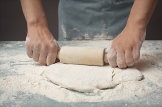 Baker rolls out dough for pizza, flatbread or pastry with rolling pin, prepare ingredients for