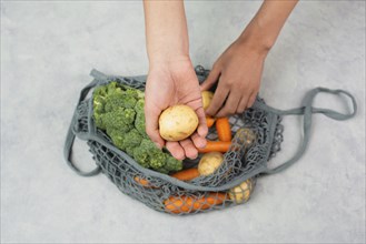 Hands taking potato from the mesh bag with vegetables, shopping grocery, healthy food ingredients,