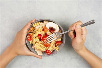 Eating a pasta salad with sliced mushroom, tomato, red pepper pieces and tuna, healthy food with