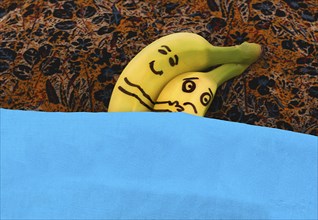 Bananas hugging each in bed. He is happy, she is sad