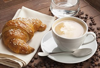 Cappuccino with croissant and glass of water in the tray of brown wood