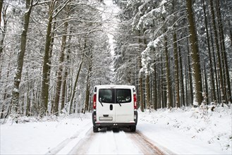 Camper Van driving on a road through a snow covered forest in winter, adventure vacation and