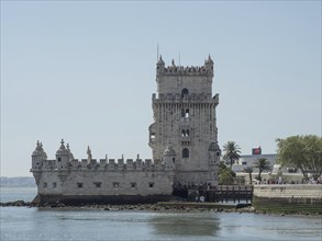 Historic stone tower on the waterfront with palm trees and clear sky in the background, Lisbon,